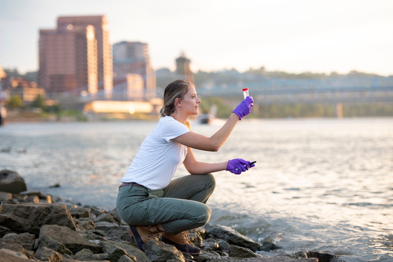 image of a student kneeling by river with a test tube of water