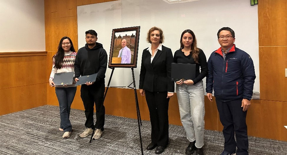 Six college students pose next to a framed portrait of Professor Dionysiou