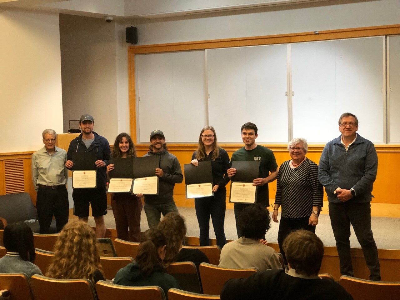 Students holding paper awards pose with faculty