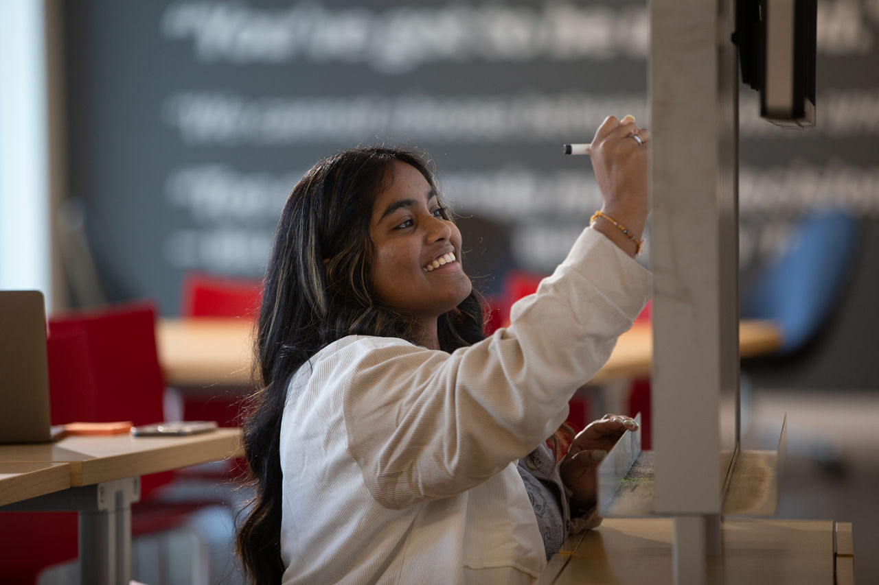 Woman smiles as she writes on a whiteboard