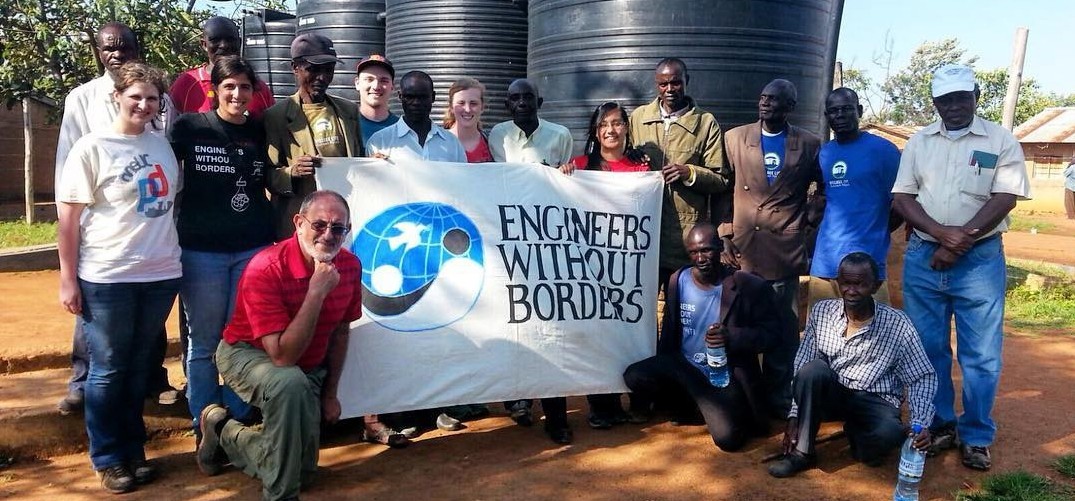 Engineers without Borders-UC Chapter poses for a picture in Tanzania with locals. They are all helping to hold the Engineers without Borders sign.